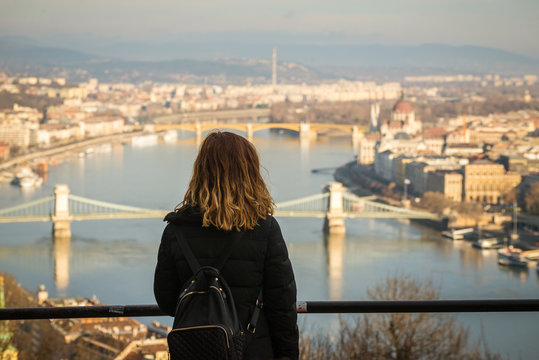 Young woman is looking at the Chain bridge, Budapest parliament and cityscape from The Citadella which is a fortification located upon the top of Gellert Hill in Budapest, Hungary.