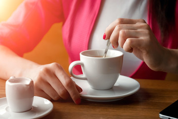 Close-up, hands of a young girl, stirs sugar in a cup of coffee, sits in a cafe behind a wooden stolikos. Business lunch, modern girl.