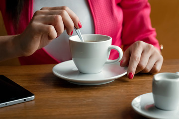 Close-up, hands of a young girl, stirs sugar in a cup of coffee, sits in a cafe behind a wooden stolikos. Business lunch, modern girl.