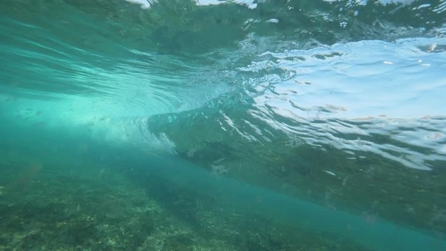 SLOW MOTION UNDERWATER: Forceful tube wave rolling towards the shore pulling behind the floating seaweed. Foam and air bubbles fill the sea floor when barrel wave breaks. Fascinating water movement.