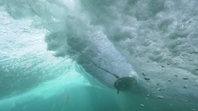 UNDERWATER SLOW MOTION: Unrecognizable extreme surfer riding glass like barrel wave filling the water with air bubbles. Adrenaline junkies fun surfing in the Canary Islands on a clear blue sunlit day.