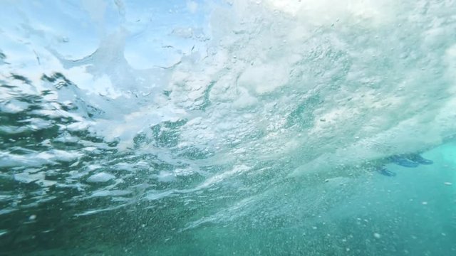 UNDERWATER SLOW MOTION Unrecognizable surfer on surfboard riding a flowing tube wave in clear blue ocean. Surfing enthusiast breaking waves on Lobos island. Thrilling Canary Islands summer vacation.