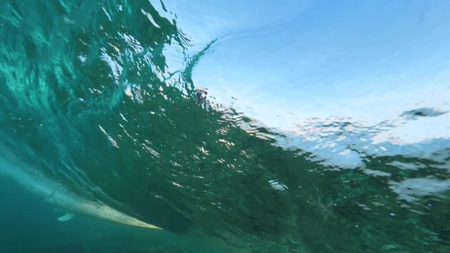 UNDERWATER SLOW MOTION: Unrecognizable pro surfer riding a beautiful glass like tube wave in a crystal clear ocean on a sunlit day in Lobos. Action packed surfing vacation in sunny Canary Islands.