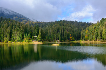 Fototapeta na wymiar View of Synevir high-altitude lake by autumn day. The leaf fall forest is reflected in water of lake.