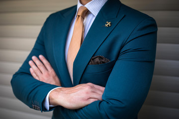 Man in custom tailored suit with athletic build posing with his hand crossed in front of background