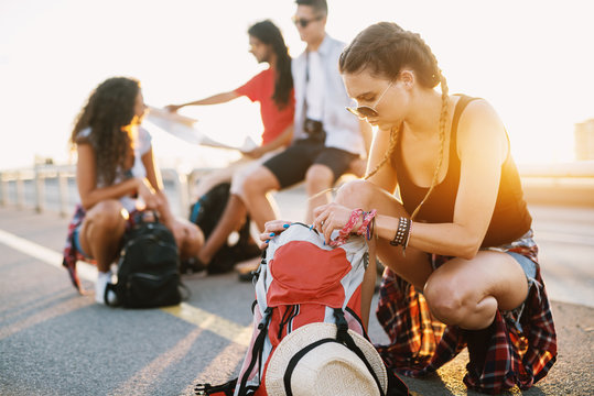 Group of four youthful tourists taking a break to repack and rest after a long walk down the streets of a new city.