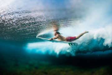 Young surfer dives under the ocean wave with surf board and performs trick named in surfing as a Duck Dive. Tilt shift effect applied
