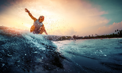 Young surfer rides the wave during sunset - obrazy, fototapety, plakaty