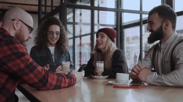 Four friends are enjoying time at the cafe, drinking coffee and laughing at the phone
