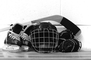 Black and white photo of kid's hockey gear: helmet, stick, gloves, skates