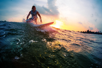 Surfer trying to catch the ocean wave during sunset. Active lifestyle and extreme sport concept