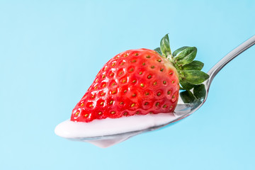 Strawberry on a spoon with strawberry pink yogurt cream close-up on blue background