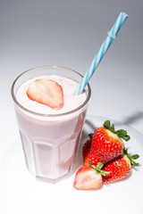 Strawberry next to a glass of strawberry yogurt close-up on a grey background