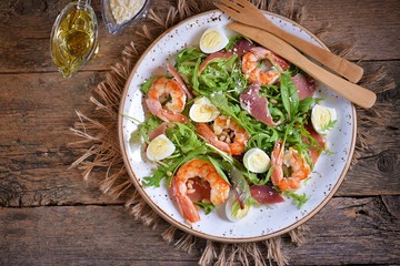 Healthy salad with shrimps, arugula, Parma ham, quail eggs and parmesan cheese.