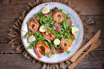 Healthy salad with shrimps, arugula, Parma ham, quail eggs and parmesan cheese.