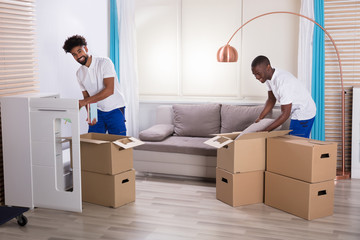 Movers Unpacking The Cardboard Boxes In The Home