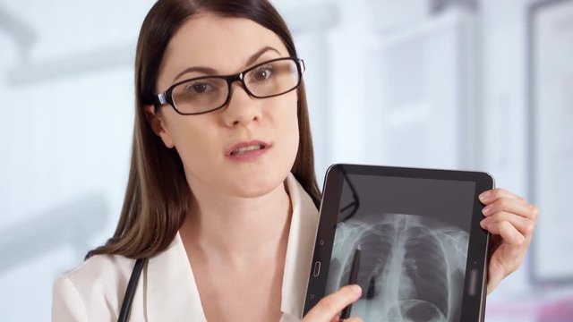 Professional female doctor with stethoscope standing in hospital room talking on phone with patient via messenger app showing X-ray, explaining diagnosis. Woman physician at work. Health care concept