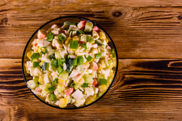 Glass bowl with salad from crab sticks on wooden table. Top view