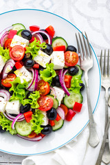 Greek salad of fresh cucumber, tomato, sweet pepper, lettuce, red onion, feta cheese and olives with olive oil. Healthy vegetarian food