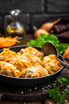 Cabbage rolls stewed with meat and vegetables in pan on dark wooden background