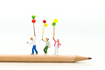 Miniature people: Childrens holding a balloon standing on a pencil. Image use for education concept.