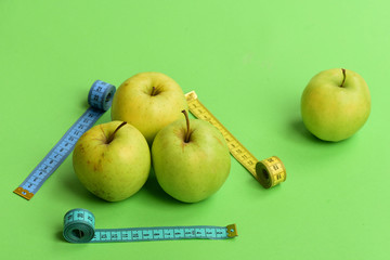 Apples near measuring tape rolls on green background, close up