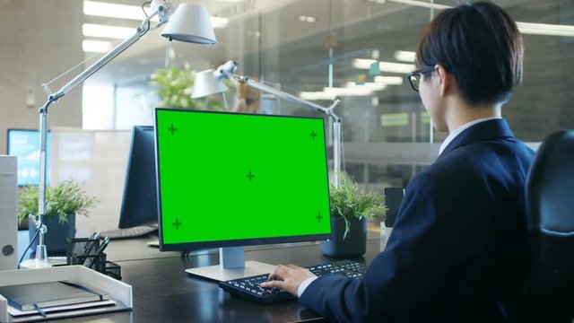 In the Office Businessman works at His Desk on a Personal Computer with Mock-up Green Screen. Colleague Enters Office and Takes Place at Her Desk.