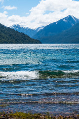 Crystal clear water of the lake with mountains on the horizon. Area of the town of Bariloche, Argentina. Focus on the foreground, on the breaking wave.