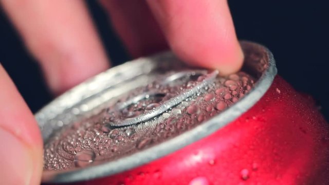 Red beverage can with soda rotates on a dark background. Water drop and bubbles. The play of light and shadow