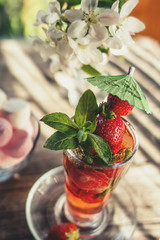 Detox drink made of ripe juicy strawberries and mint in a transparent glass Cup on the background of marshmallows and a bouquet of white flowers on a wooden table on a Sunny day. Selective focus.