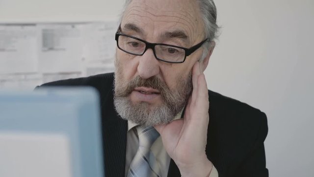 Tired sad senior businessman works with pc in office. 4K