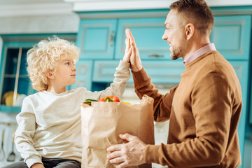 Family relations. Positive nice happy father and son smiling and giving each other a high five while being a team