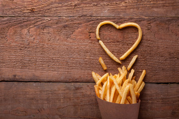 I love fried potatoes. French fries in a paper box and symbol of a heart on a wooden table