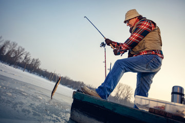 Fisherman catch fish pike on the frozen river in winter
