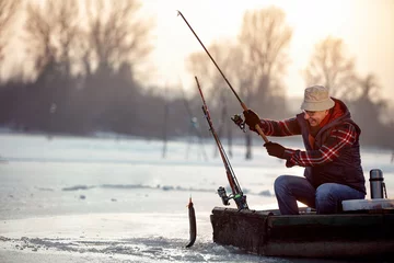 Photo sur Plexiglas Pêcher pêche sur glace sur un lac gelé - un pêcheur souriant attrape du poisson