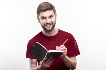 Pleasure to create. Cheerful young man making notes in his planner and smiling at the camera joyfully while posing isolated on a white background