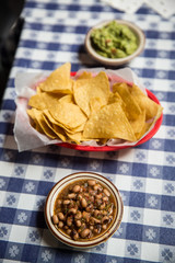 Black beans, chips and guacamole on a blue checkered tablecloth