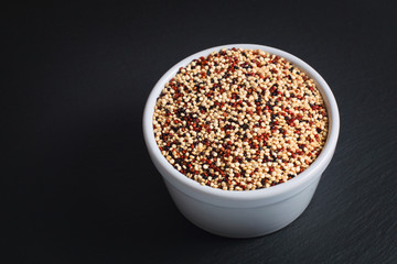 Healthy food  concept Organic raw Quinoa grain mix of 3 colours white, red and black in white ceramic cup on black slate stone plate with copy space 