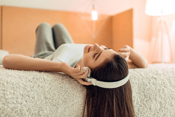 Favorite music. Beautiful teenage girl lying on her bed and listening to the music in the headphones while closing the eyes and enjoying peacefully
