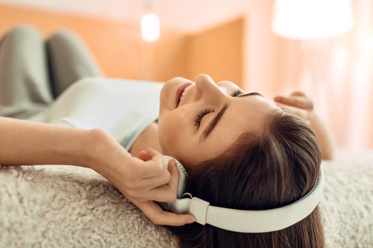 Relaxing song. The close up of a pretty teenage girl lying on the bed and listening to the music in the headphones while relaxing with closed eyes