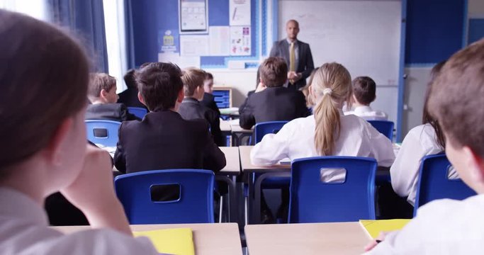 4k, Group of school kids sitting and listening to teacher in classroom from back