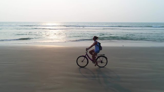 A young women rides a bike on a sandy beach in the rays of sun. Drone shooting.