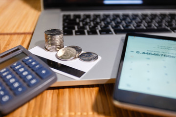 A stack of coins on credit cards next to the smartphone with a calculator app on the background of a notebook with the personal cabinet of the Internet Bank. Wooden office desk. Top view,flat lay