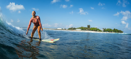 Happy surfer rides the ocean wave and smiles. Perfect sunny day, crystal clear water and tropical island on the background