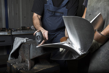 two man work with anvil and hammer on boat propeller