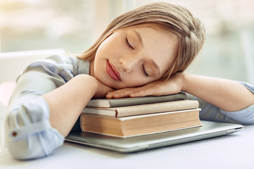 Sweet rest. Charming teenage girl taking a nap while sitting at the table and resting her head on the hands folded on a pile of books