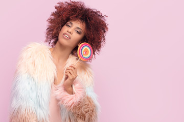 Fashionable afro woman with lollipop on pink background.