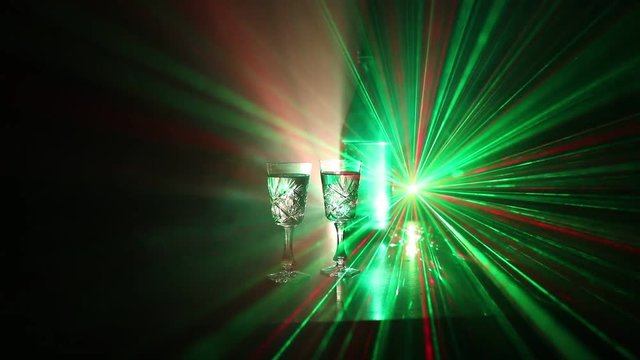 Two glasses of Vodka with bottle on dark foggy club style background with glowing lights (Laser, Stobe) Multi colored. Club drinks theme decoration. Empty space. Selective focus