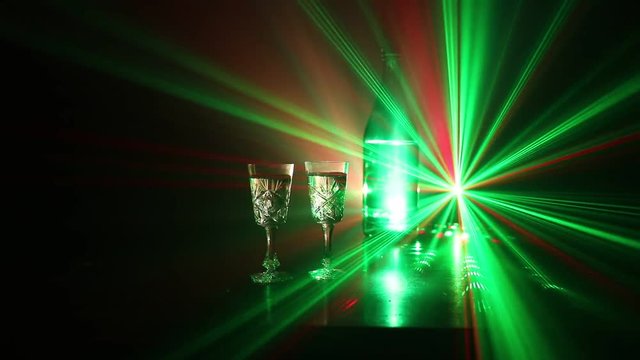 Two glasses of Vodka with bottle on dark foggy club style background with glowing lights (Laser, Stobe) Multi colored. Club drinks theme decoration. Empty space. Selective focus