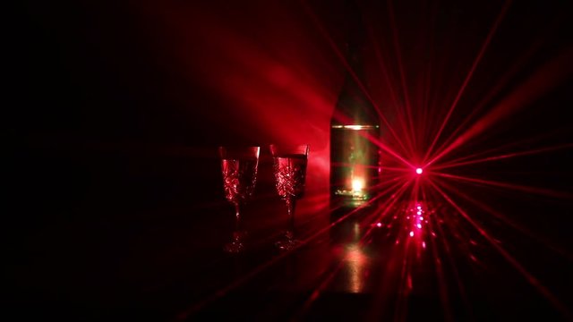 Two glasses of Vodka with bottle on dark foggy club style background with glowing lights (Laser, Stobe) Multi colored. Club drinks theme decoration. Empty space. Selective focus